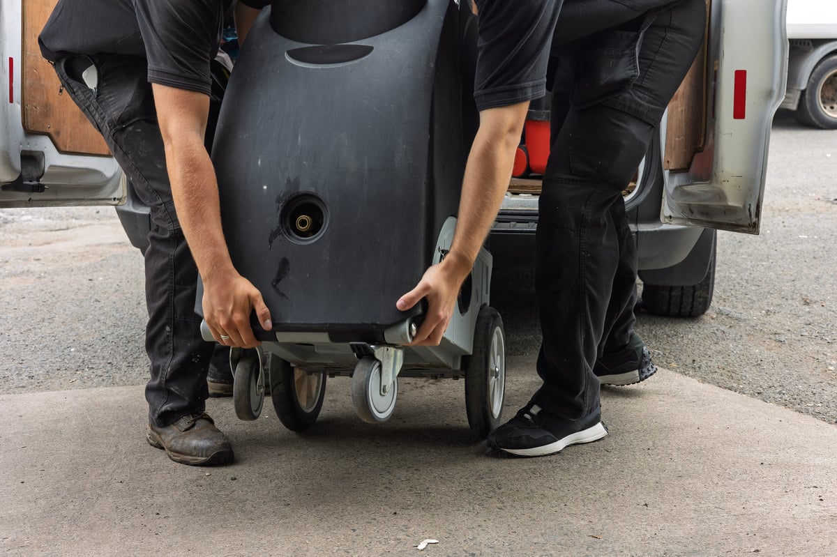Two workers lowering an industrial cleaning machine from a service van